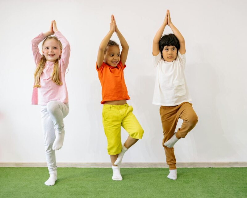 Three diverse children practicing yoga indoors, showcasing joy and balance.